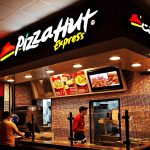 Man in black t shirt next to pepperoni pizza