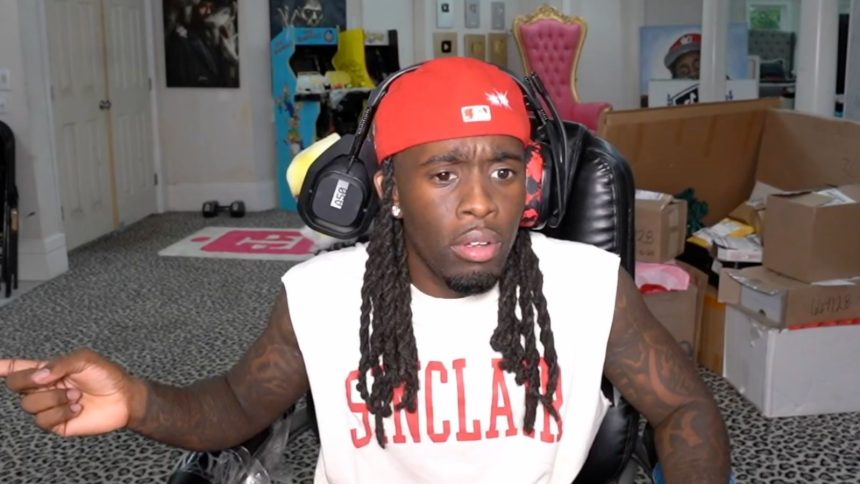 Kai Cenat in red hat pointing off screen