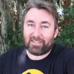 Adam The Woo in black and yellow shirt talking to camera