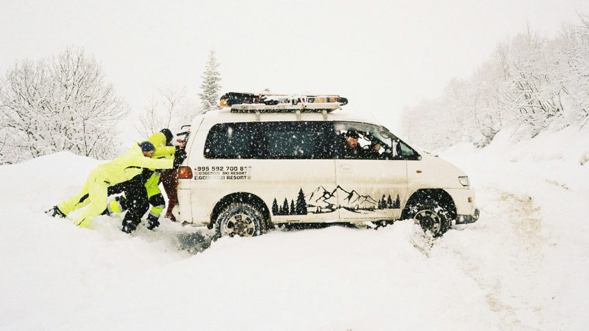 Two people push a stuck van in the snow.