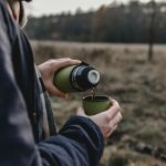 Person pouring drink through green thermos