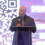 Pastor Hall talking in front of screen with QR code on