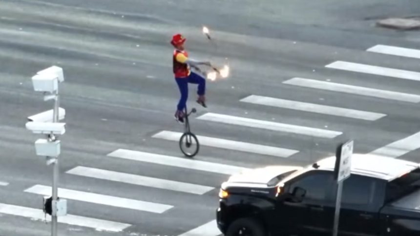 man juggles fire on unicycle in intersection