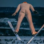 Man in white suit flying through sky on skis