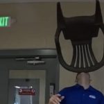 Man in blue shirt balancing green chair on chin