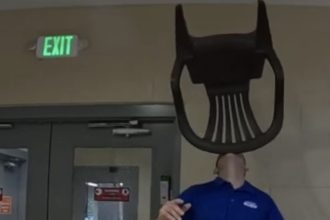 Man in blue shirt balancing green chair on chin