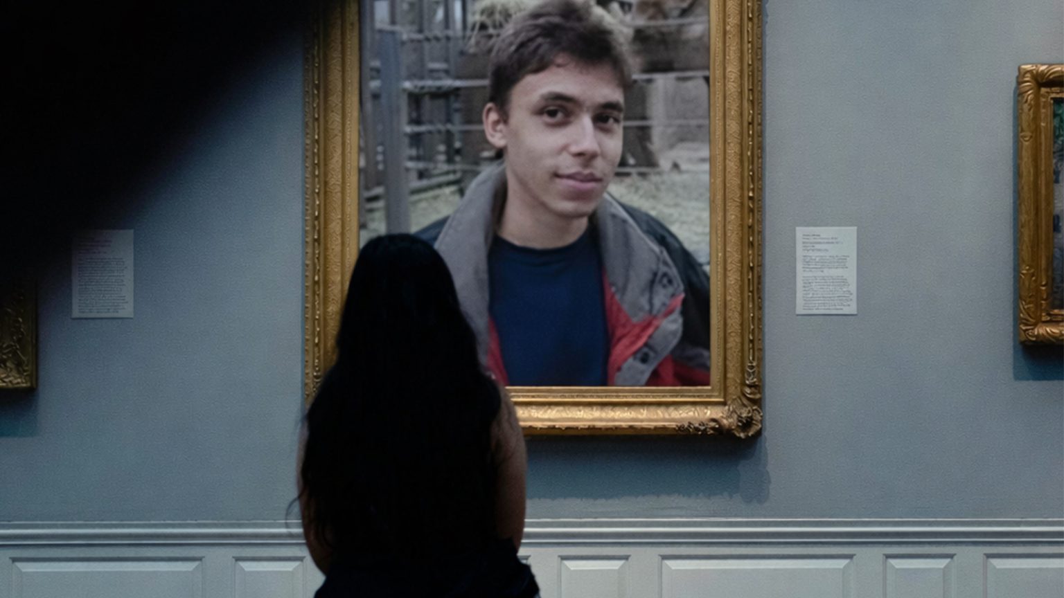 A woman sits in a museum looking at a picture frame with Jawed in 'Me at the zoo.'